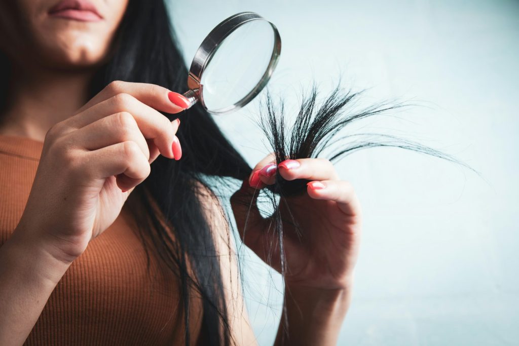 Une femme examine les pointes fourchues de ses cheveux à la loupe.